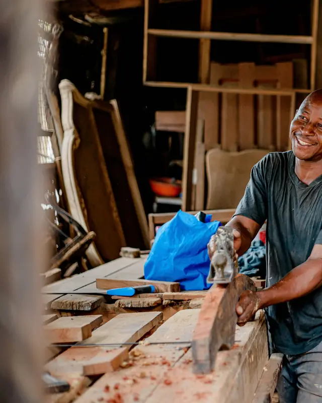 Un artisan souriant à son établi, dans son atelier de menuiserie.